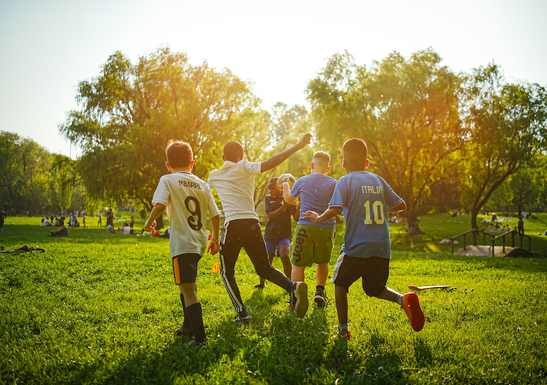 Kids chasing a soccer ball across a sunny park field